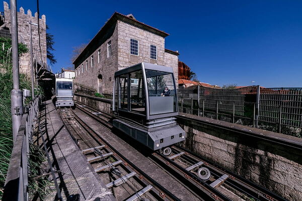 Two funicular cars await eager passengers beside historic buildings under a clear blue sky in Porto. (Text KI-generiert)