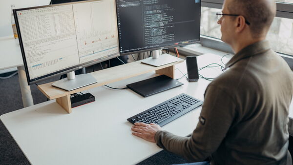 A man analyzes data on dual monitors while coding at a desk in a modern office setting. (Text KI-generiert)